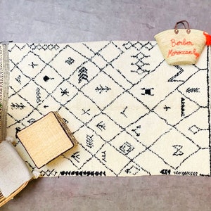 May include: A white and black Moroccan rug with geometric patterns and fringe. A woven basket bag with the text "Borber Moroccan Bag" is on the rug.