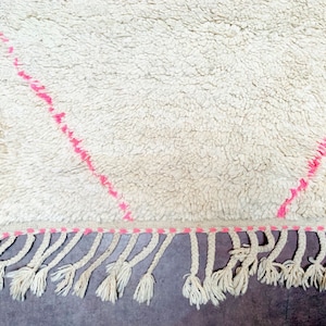 May include: White shag rug with pink diamond pattern and fringe. The rug has a soft, fluffy texture.