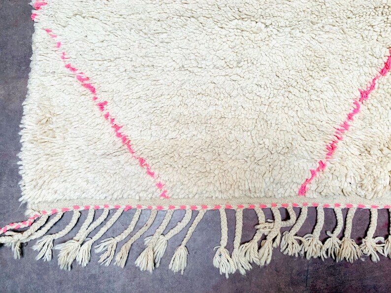May include: White shag rug with pink diamond pattern and fringe. The rug has a soft, fluffy texture.