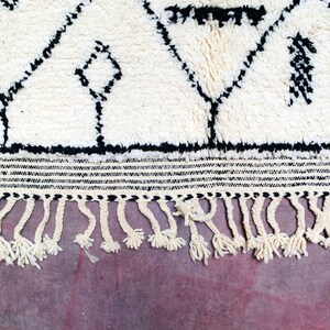 May include: White and black Moroccan rug with a geometric pattern and fringe. The rug has a thick, fluffy pile.