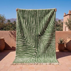 May include: A green and white patterned rug with a textured surface. The rug features a repeating linear design and a fringed edge. The rug is displayed outdoors on a sunny day.