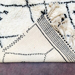 May include: A white and black geometric patterned rug with fringe. The rug is folded in half and the fringe is visible.