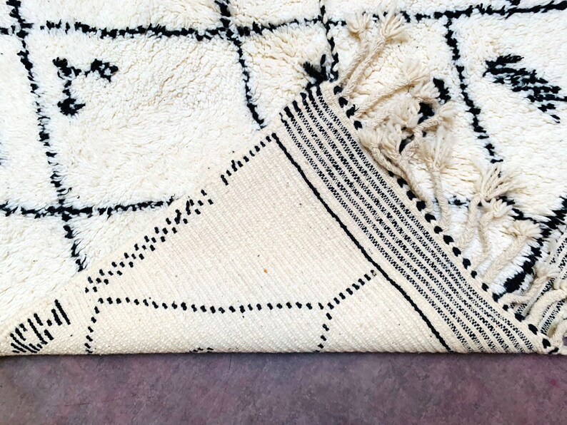May include: A white and black geometric patterned rug with fringe. The rug is folded in half and the fringe is visible.