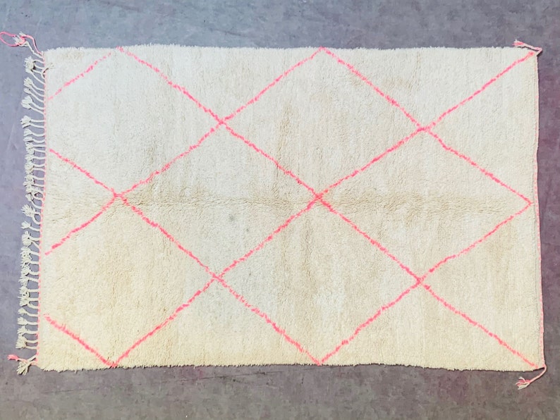 May include: A white rug with a diamond pattern in pink. The rug has a fringe border.