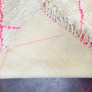May include: A white rug with pink stitching, folded to show the underside. The rug has a fringe border.