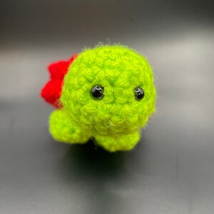 May include: A small green crocheted turtle with red accents and black eyes.