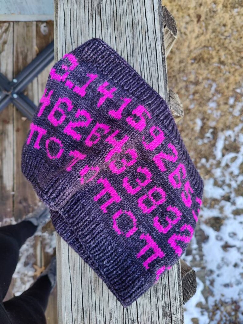 May include: A dark gray knitted headband with a pink alphabet pattern. The headband is made of a soft, comfortable material and is perfect for keeping your ears warm in the winter.