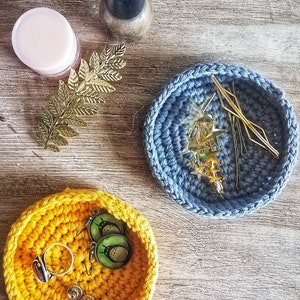 May include: Two crocheted bowls, one yellow and one blue, with various small items inside. The yellow bowl contains earrings and a ring, while the blue bowl holds hair clips and bobby pins.