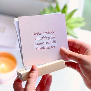 positive daily affirmations pack held in wooden holder on woman's desk