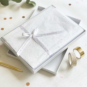 a personalised scrapbook in white and gold gift wrap with a ribbon and bow inside a gift box