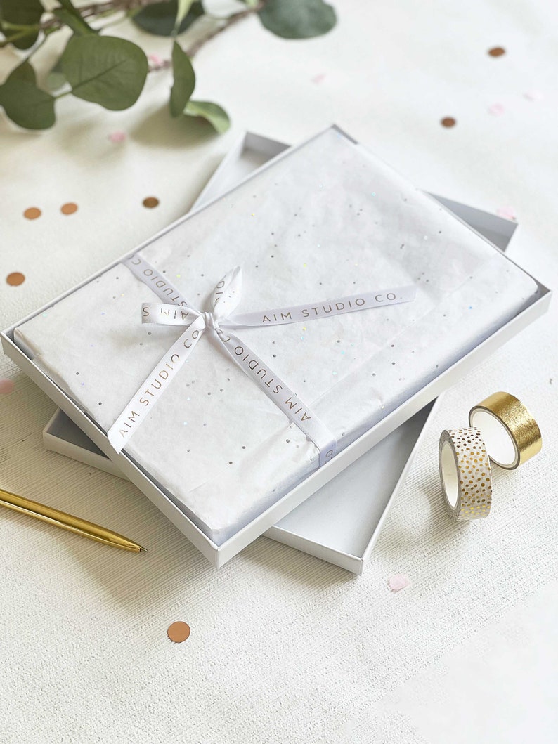a personalised scrapbook in white and gold gift wrap with a ribbon and bow inside a gift box