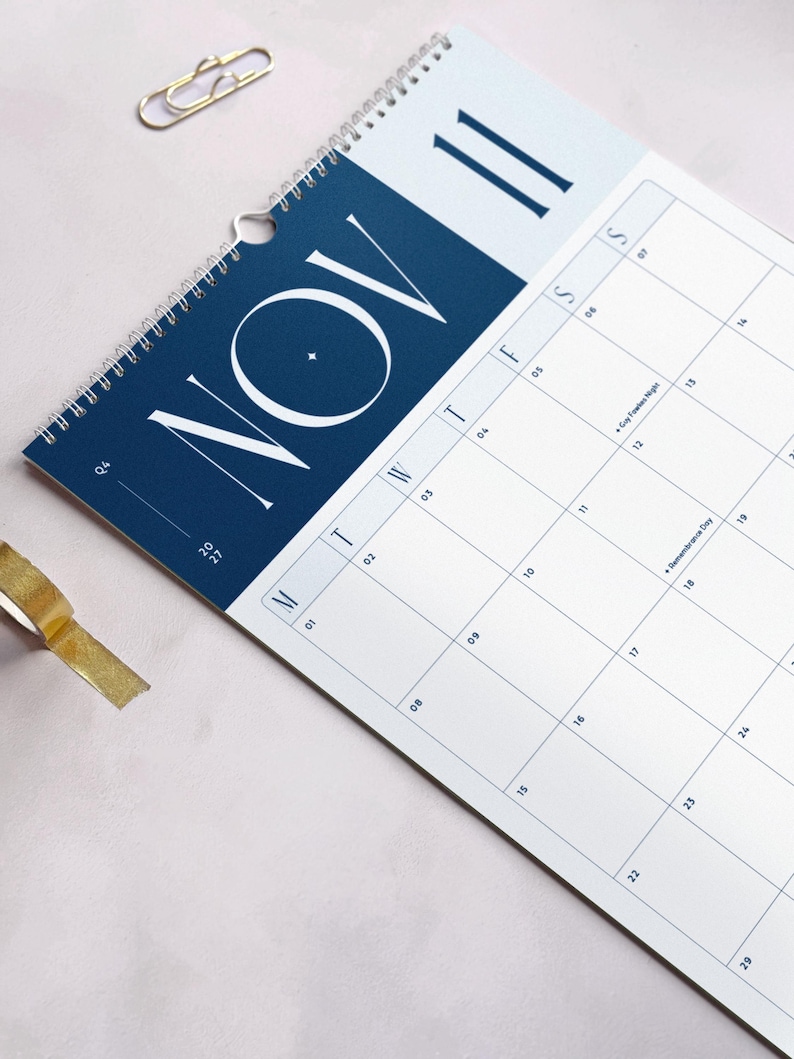 Close up of a monthly calendar showing November 2027 on a light background. The header has large Monday-start planner grid and a bold blue header with modern typography.