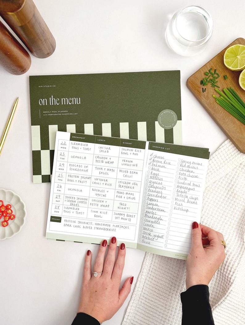 A4 notepad with cover showing weekly menu planner with perforated shopping list. A woman is using the tear-off design to detach the grocery list section.