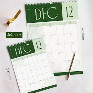 2027 month view calendar showing December with sage green and deep forest green heading and large typographic design. The calendars are on a light surface with large A3 and small A4 size dimensions to show scale between the two options.