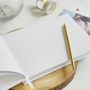 detailed image showing close up plain pages of an anniversary memory book and gold pen resting on the open blank page.