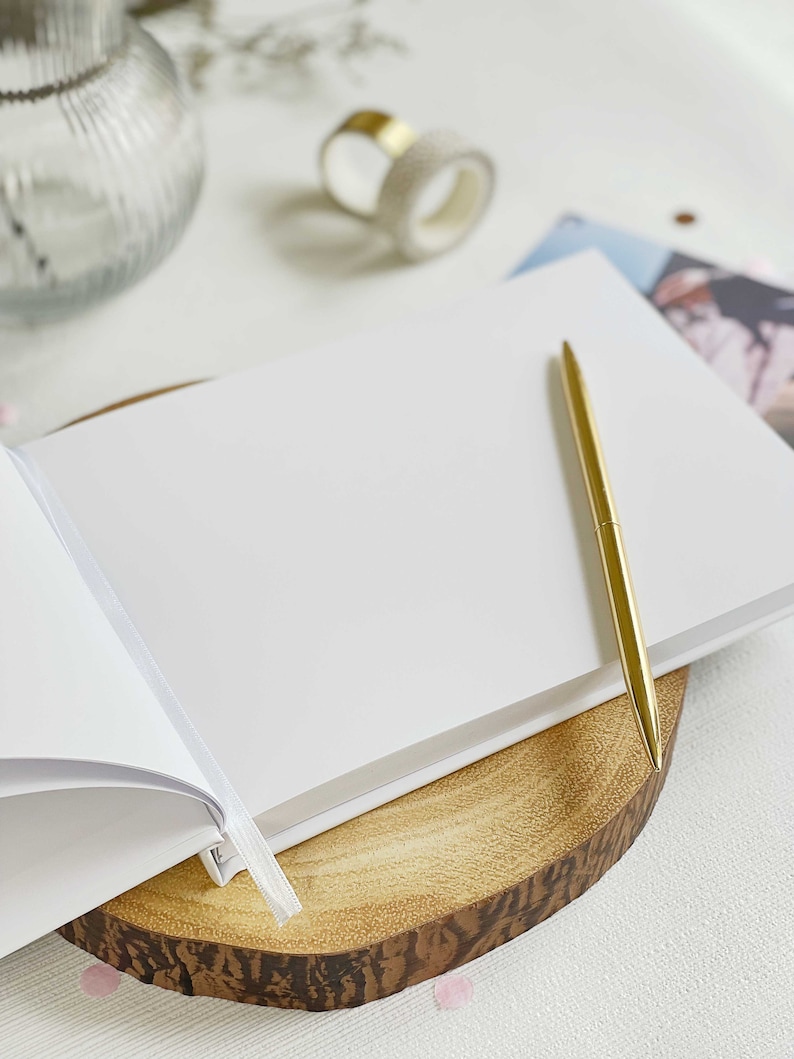 detailed image showing close up plain pages of an anniversary memory book and gold pen resting on the open blank page.