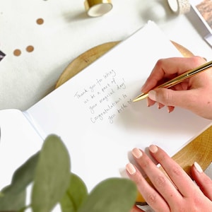 wedding guest writing message to married couple on their wedding day in a blank guest book.