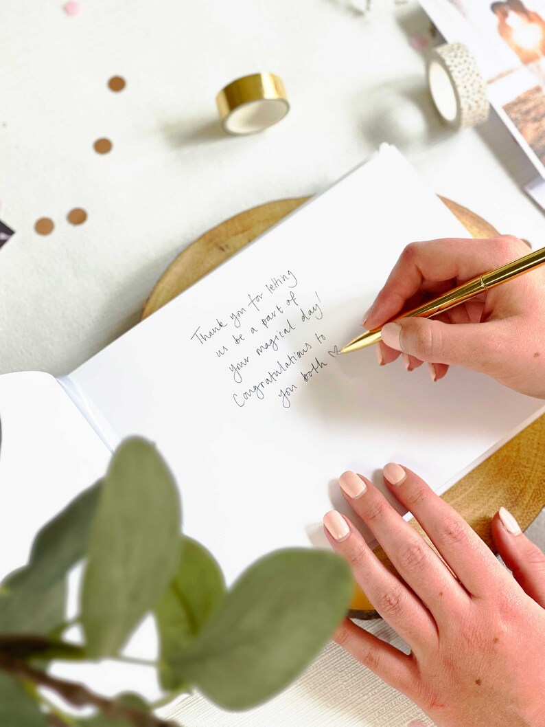 wedding guest writing message to married couple on their wedding day in a blank guest book.