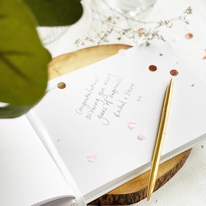 a wedding guest book with the page open showing handwritten guest message and slim gold pen resting on the page