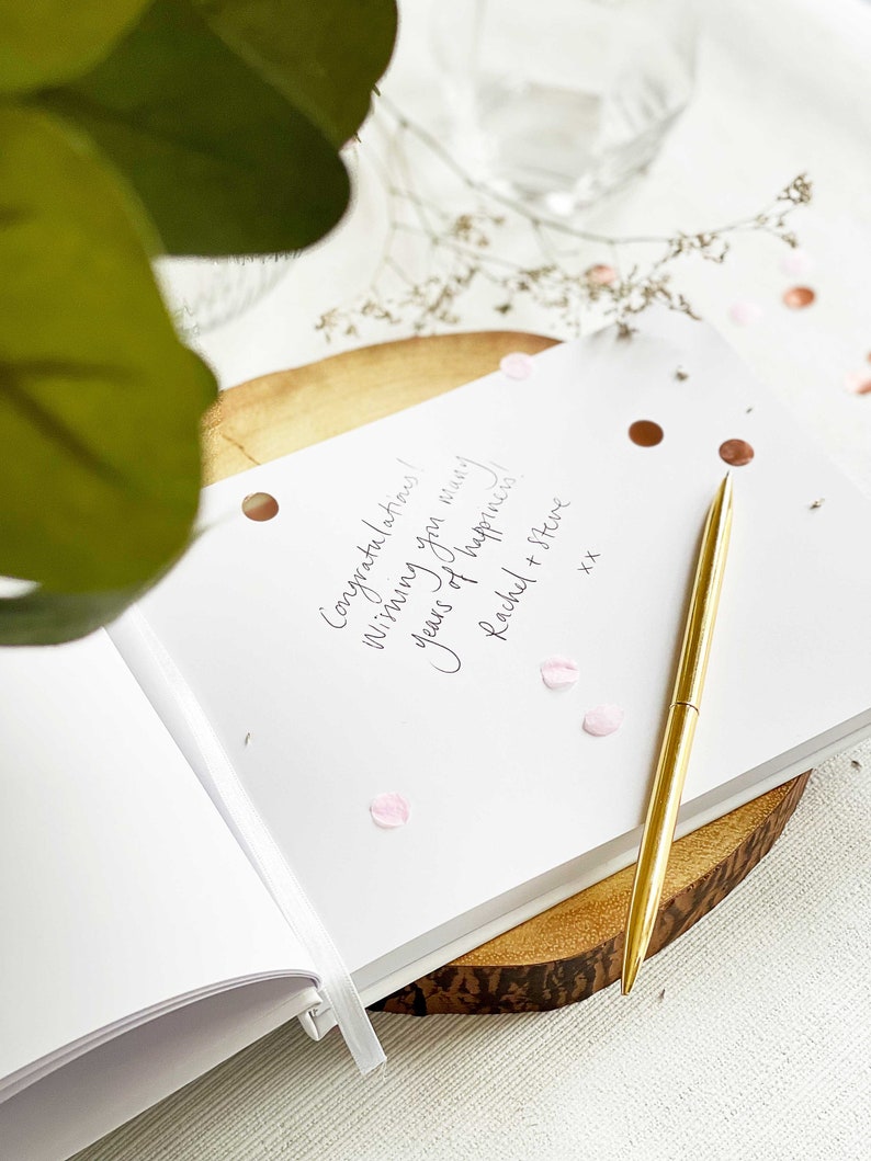 a wedding guest book with the page open showing handwritten guest message and slim gold pen resting on the page