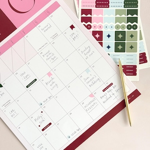 january calendar page on a desk with handwritten plans filled out across the monthly calendar page. A gold pen lies across the corner of the planner, and there are matching sticker sheets next to the calendar and used within the aesthetic layout.