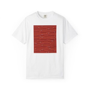 以下が含まれることがあります： 白い半袖Tシャツで、中央に長方形のグラフィックが配置されています。濃い赤の水平線にオレンジと白のダッシュが断続的に入っており、胸元にテクスチャのあるグリッチのようなパターンを作り出しています。