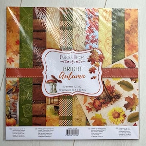 May include: A package of decorative paper sheets with an autumn theme. The package features the text "BRIGHT Autumn" and includes 10 double-sided sheets, each measuring 12x12 inches. The paper has various designs with leaves, pumpkins, and wood textures.