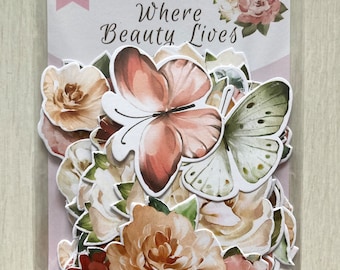 Peut inclure: Un paquet de 54 embellissements en papier floral et papillon. Le paquet est étiqueté "Fabrika Decoru" et "Where Beauty Lives". Les embellissements sont dans des tons de rose, blanc, vert et marron.