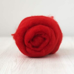 Puede incluir: Primer plano de una bola de fibra de lana de color rojo brillante. La lana es suave y esponjosa, y es perfecta para el fieltro o el hilado.