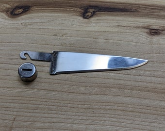 May include: A silver knife with a hook on the handle and a small silver cap with a slot in the center.