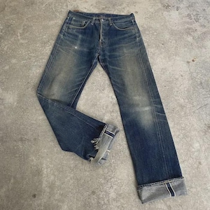 May include: Faded blue denim jeans with a button fly and classic five-pocket design. The jeans have a worn appearance with distressed details at the cuffs and knees. The cuffs are turned up, revealing a contrasting fabric.