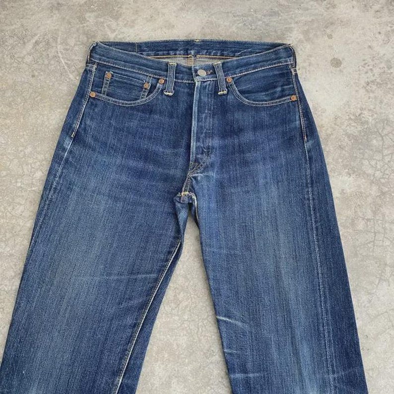 May include: Blue denim jeans with a button fly, five-pocket design, and a faded wash. The jeans have a classic straight-leg fit and are made of durable denim material. The jeans are a medium wash blue color.