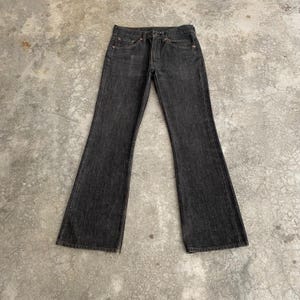 Puede incluir: Vaqueros de mezclilla gris oscuro con un diseño de pierna acampanada. Los vaqueros tienen un estilo clásico de cinco bolsillos, cierre de botón y cremallera, y trabillas para el cinturón. La tela parece desgastada, dando a los vaqueros un aspecto vintage.