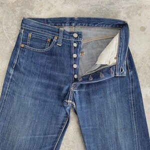 May include: Blue denim jeans with a button fly. The jeans have a classic five-pocket design, with rivets at the corners of the pockets. The denim has a faded appearance, suggesting wear. The jeans are unbuttoned, showing the interior.