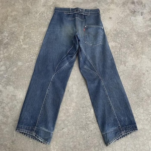 Puede incluir: Vaqueros azules de mezclilla con un diseño de pierna ancha. Los vaqueros tienen un bolsillo trasero con una etiqueta roja de Levi's. Costuras visibles y apariencia vintage o desgastada. La cintura tiene trabillas.