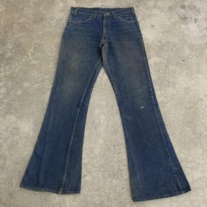 May include: A pair of vintage blue denim bell-bottom jeans. The jeans have a classic five-pocket design, a button and zipper closure, and a faded wash. The flared legs are a prominent feature of the jeans.