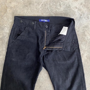 May include: Black corduroy pants with a button and zipper closure. The pants have a classic five-pocket design and a straight leg fit. The label reads "JUNYA WATANABE MAN".