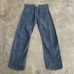 Puede incluir: Unos pantalones vaqueros de mezclilla azul con lavado medio, diseño de cintura alta, cierre de botones y perneras anchas. Los pantalones tienen una costura vertical visible en la parte delantera de cada pierna y un dobladillo ancho en el bajo.