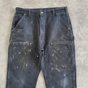 Puede incluir: Pantalones de trabajo azul marino oscuro con m&uacute;ltiples bolsillos y detalles de remaches. Los pantalones muestran signos de desgaste con salpicaduras de pintura, lo que sugiere su uso en un entorno de trabajo. Cierre con bot&oacute;n y cremallera.