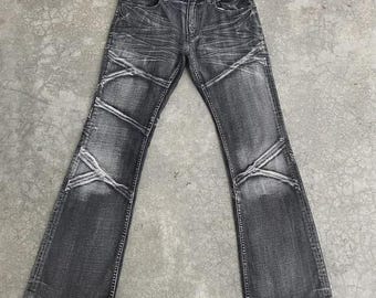 May include: A pair of distressed black denim jeans with a faded, worn appearance. The jeans feature a unique design with white stitching and accents across the knees and thighs. The jeans have a classic five-pocket design and a bootcut leg opening.