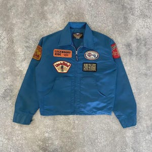 以下が含まれることがあります： ジッパーフロントと複数の刺繍パッチが付いた、ティールブルーのジャケット。「Legendary Ride」と「Ride to Live, Live to Ride」というフレーズを含むパッチ。ジャケットには2つのフロントポケットと襟が付いています。背面にハーレーダビッドソンのロゴ。