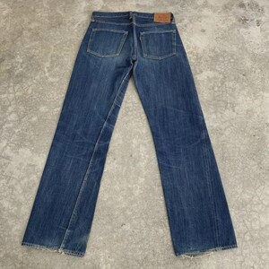 May include: A pair of blue denim jeans, viewed from the back, with two back pockets and a small leather patch. The jeans have a classic five-pocket design and a straight leg fit. The denim shows signs of wear and fading.