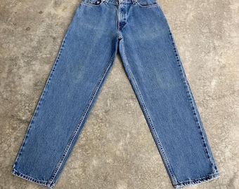May include: Light blue denim jeans with a classic five-pocket design. The jeans have a straight leg cut and a button and zip closure. The denim has a faded appearance, with subtle wear marks. The jeans are laid flat on a neutral surface.