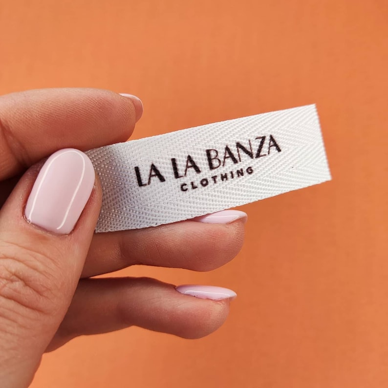 May include: White woven clothing label with the text "LA LA BANZA CLOTHING" printed in brown.