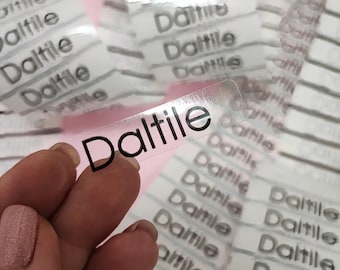 May include: A close-up of a clear sticker with the word "Daltile" printed in black. The sticker is on a roll of similar stickers.