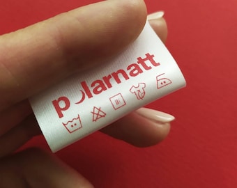 May include: White clothing label with red text that reads "polarnatt" and red care instructions symbols. The symbols include a washing machine, a triangle with an X, a square with two vertical lines, a t-shirt, and an iron with two dots.