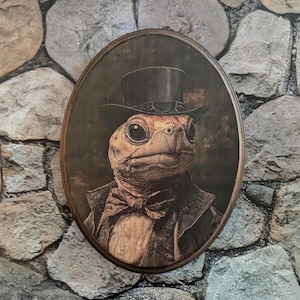 May include: A round wooden plaque featuring a portrait of a turtle wearing a top hat and bow tie. The turtle has a serious expression and is looking directly at the viewer.