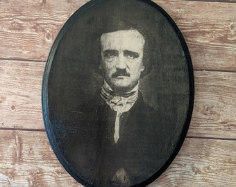 May include: A black and white portrait of a man with a mustache and goatee, wearing a dark suit and a white collar. The portrait is framed in a black oval frame.