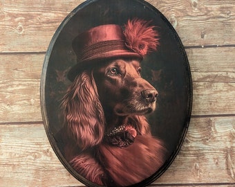 May include: A brown and white dog wearing a red hat with a feather on top. The dog is looking to the right and has a serious expression. The image is in a circular frame.