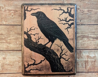 May include: A black crow perched on a branch of a bare tree, with a woodgrain background. The crow is facing left and the tree branches are silhouetted against a light brown background.